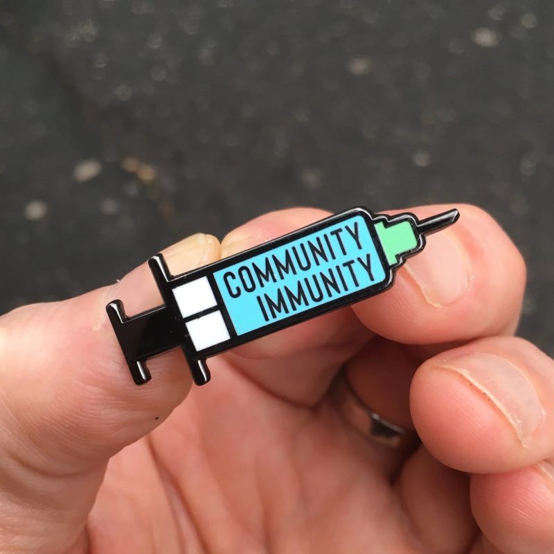 Community Immunity Syringe Pin in hand